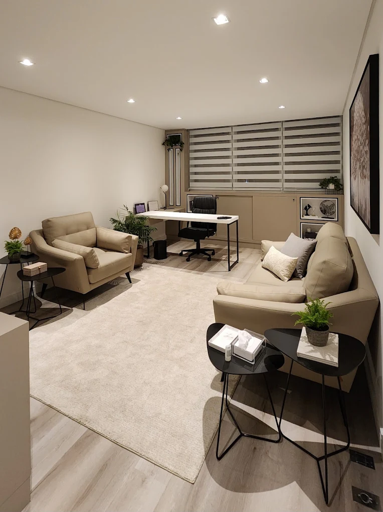 Sala de atendimento com poltronas bege, tapete claro e plantas
